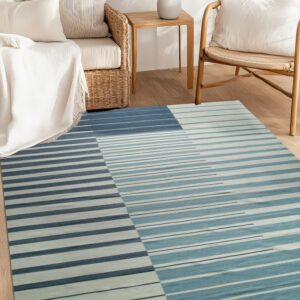 Blue and teal striped rug on wood flooring in a neutral room with woven rattan sofa and chair.