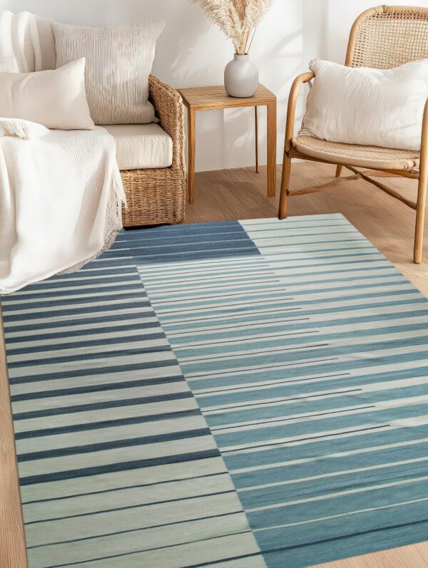 Blue and teal striped rug on wood flooring in a neutral room with woven rattan sofa and chair.