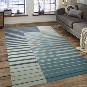Abstract striped rug in varying blue and white tones segments the rustic wood flooring next to a gray sofa.