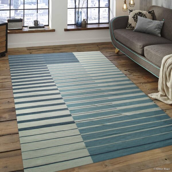 Abstract striped rug in varying blue and white tones segments the rustic wood flooring next to a gray sofa.
