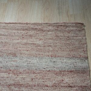 Speckled flat-weave rug with variegated pink and cream horizontal bands on light wood plank flooring.