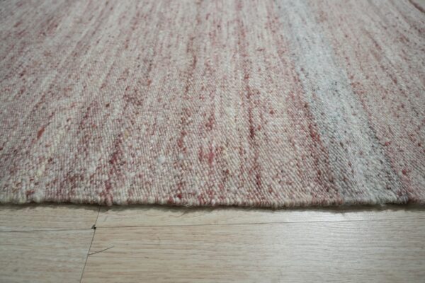 Chunky woven rug featuring a variegated white and reddish-brown speckled texture on light wood planks.
