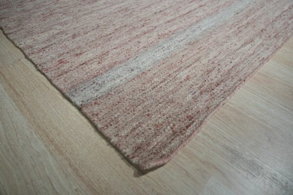 A diagonally striped pink and cream textured rug rests on light wood flooring.