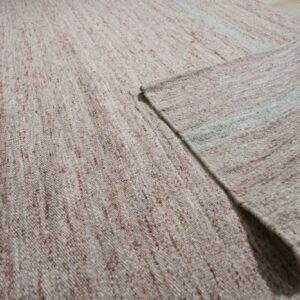 Close-up of a heathered pink and cream flatweave rug folded on light wood plank flooring.