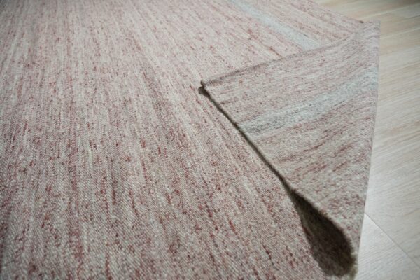 Close-up of a heathered pink and cream flatweave rug folded on light wood plank flooring.