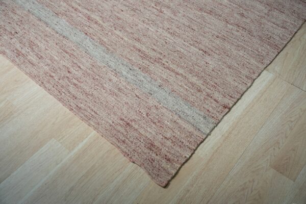 Speckled pink and cream flatweave rug with a light gray stripe shown on light wood floors.