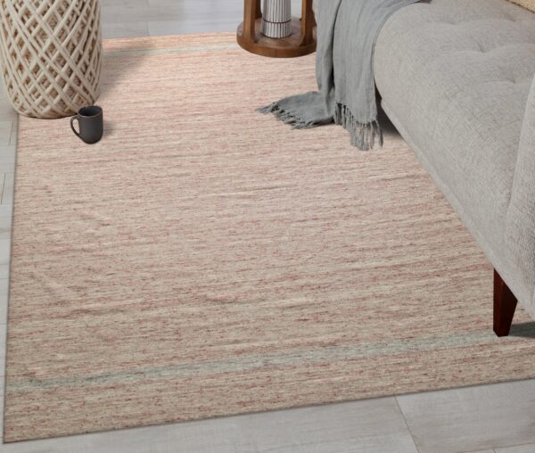 Heathered pink and cream low-pile rug lying on light plank flooring beneath a beige upholstered sofa.