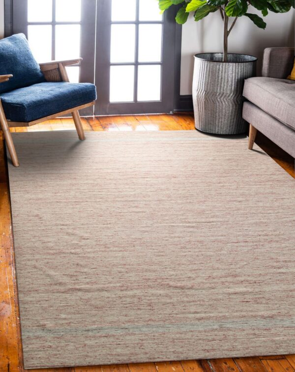 Low-pile dusty rose rug sits on wood floors beneath a blue armchair and a gray couch.