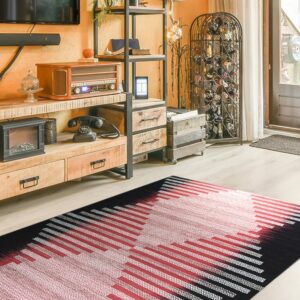 Black, red, and white geometric flatweave rug on light wood flooring beneath an industrial shelf unit.