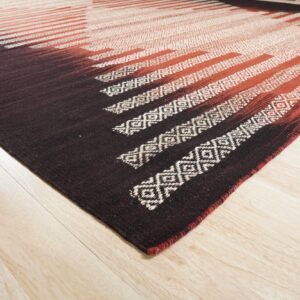 Flatwoven rug in dark brown, rust, and white geometric stripes rests on blonde wood planks.
