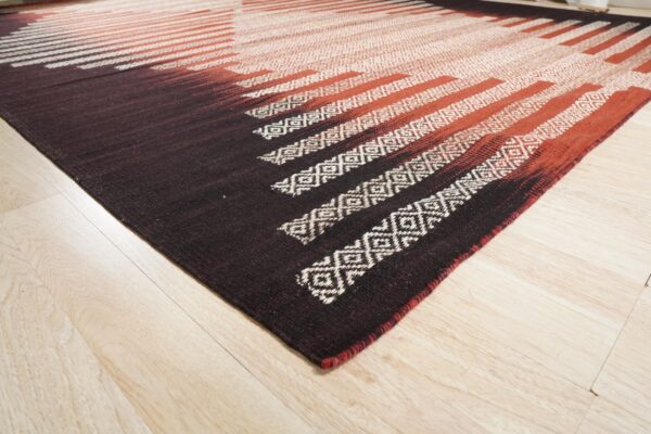 Flatwoven rug in dark brown, rust, and white geometric stripes rests on blonde wood planks.