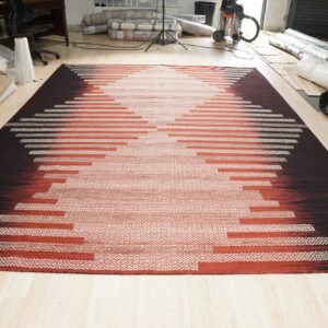 Flatweave rug with a stepped geometric pattern transitioning from dark brown to cream on light wood flooring.