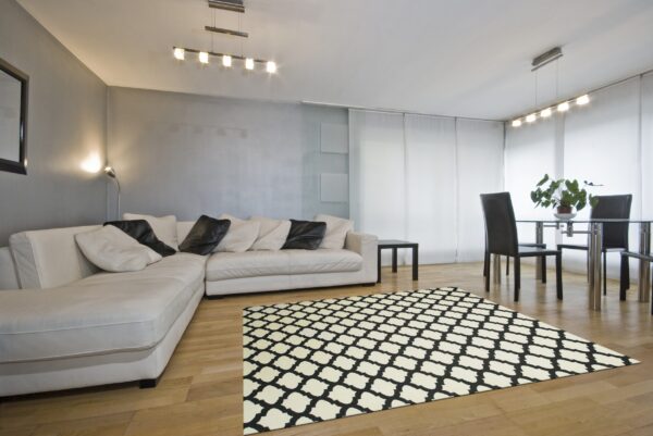 Black and cream quatrefoil rug on wood flooring in a modern living and dining room.