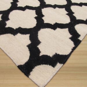 Textured black and cream rug with a geometric quatrefoil pattern shown on light wood flooring.