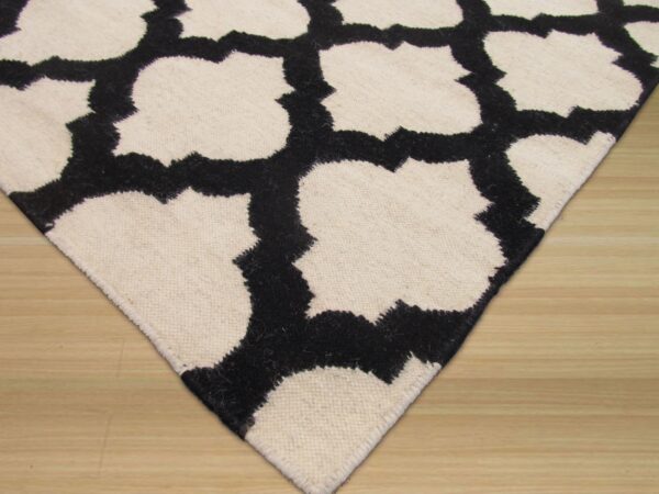 Textured black and cream rug with a geometric quatrefoil pattern shown on light wood flooring.
