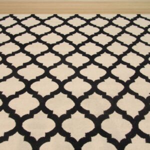 A cream rug with a black geometric trellis pattern covers light natural wood flooring.