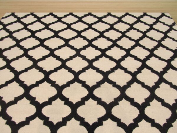 A cream rug with a black geometric trellis pattern covers light natural wood flooring.