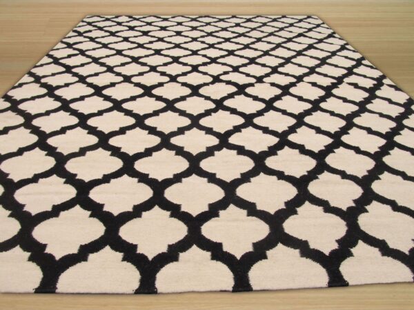 A black and cream rug featuring a repeating geometric lattice pattern on light wood flooring.