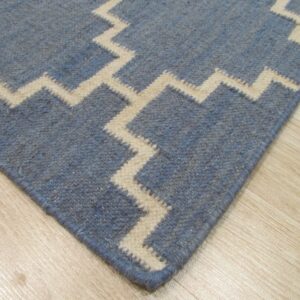 A blue rug featuring a bold cream zigzag pattern is displayed closely on light wood flooring.
