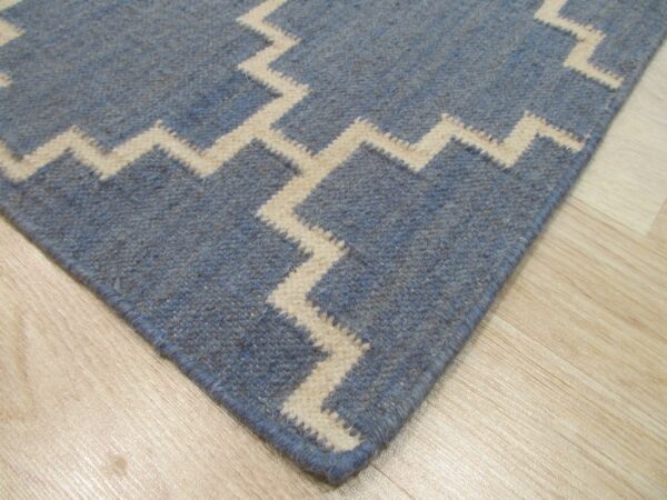 A blue rug featuring a bold cream zigzag pattern is displayed closely on light wood flooring.