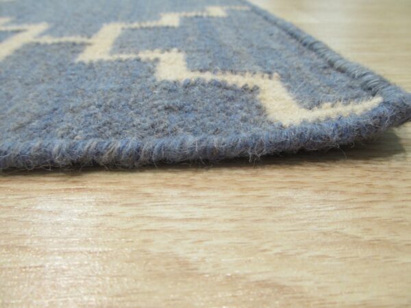 Close-up of a shaggy blue rug with a cream geometric pattern on light blonde wood flooring.