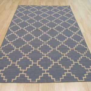 Blue flatweave rug with a repeating stepped beige trellis pattern on light blonde wooden floor.