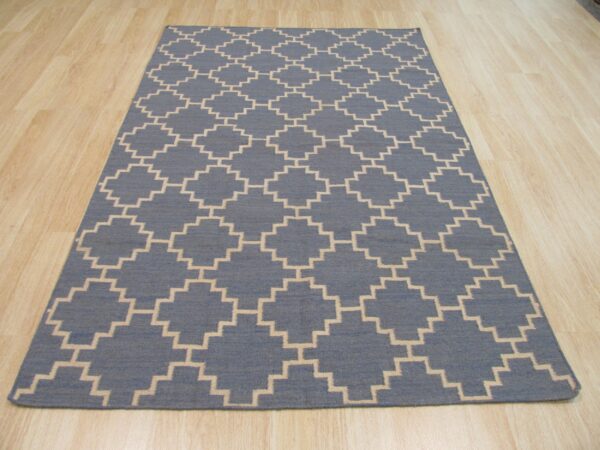 Blue flatweave rug with a repeating stepped beige trellis pattern on light blonde wooden floor.
