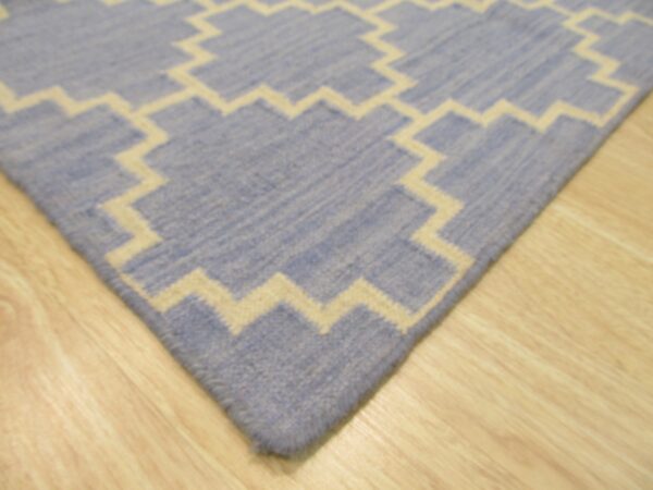 Low-pile blue rug with a cream stepped geometric pattern rests on light wood flooring.
