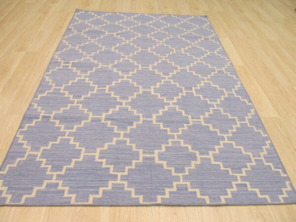 Blue rug featuring a repeating cream stepped trellis pattern displayed on light wood flooring.