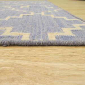 Low-angle view of a blue and cream geometric patterned rug edge on light wood flooring.