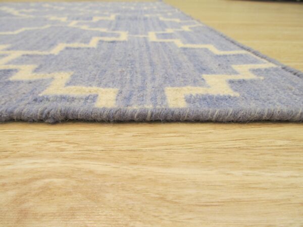Low-angle view of a blue and cream geometric patterned rug edge on light wood flooring.