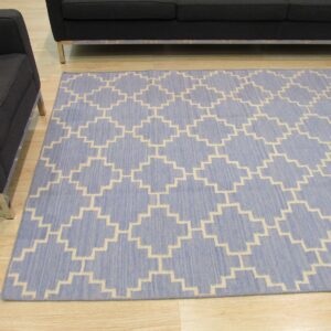 Blue and cream flat-woven rug with a trellis pattern on light wood floors near dark gray seating.