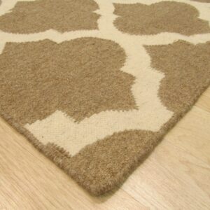 The corner of a tan and cream high-low pile rug featuring a large quatrefoil pattern on light wood flooring.