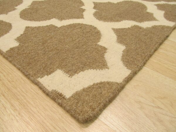 The corner of a tan and cream high-low pile rug featuring a large quatrefoil pattern on light wood flooring.