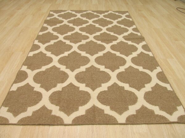 Tan and beige low-pile rug with a repeating quatrefoil pattern lies on light wood flooring.