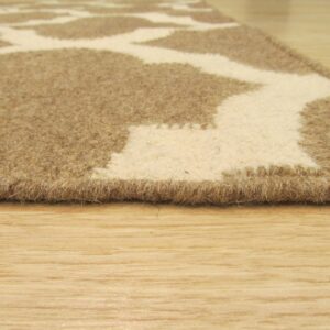 The edge of a medium-pile rug with a beige and brown organic pattern sits on light wood planks.
