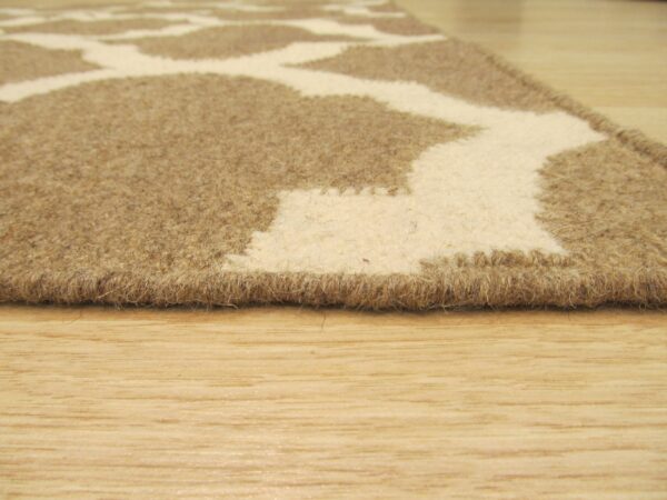 The edge of a medium-pile rug with a beige and brown organic pattern sits on light wood planks.