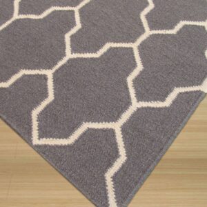 A dark gray rug with a cream geometric lattice pattern lies on light wood flooring.