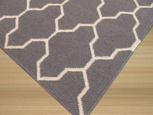 A dark gray rug with a cream geometric lattice pattern lies on light wood flooring.