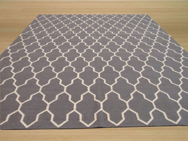 A gray rug with a white geometric trellis pattern lies flat on light blonde wood flooring.