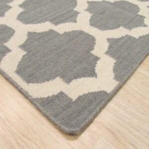 Gray and white low-pile rug featuring a large interlocking geometric pattern on light hardwood flooring.