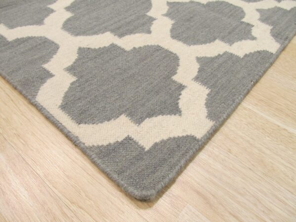 Gray and white low-pile rug featuring a large interlocking geometric pattern on light hardwood flooring.