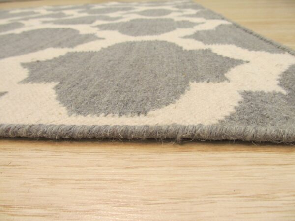 Close-up shows a thick grey and cream patterned rug edge resting on light wood flooring.
