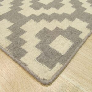 Corner view of a gray and cream geometric low pile rug on light wood flooring.