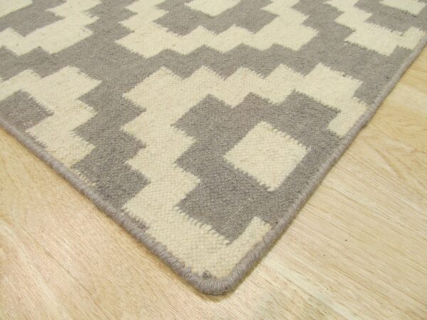 Corner view of a gray and cream geometric low pile rug on light wood flooring.