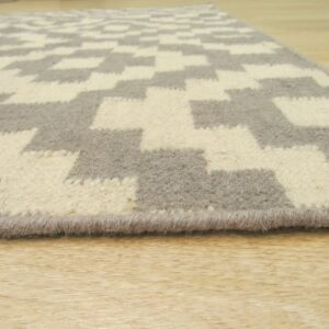 Low-pile rug in cream and taupe geometric pattern sits on shiny light-colored wooden flooring.