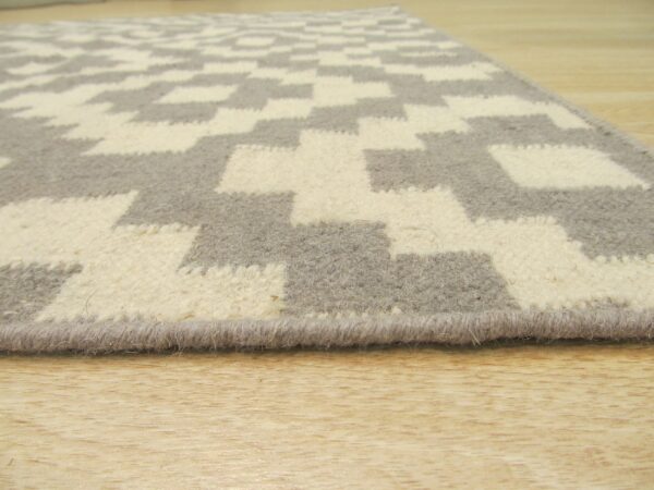 Close-up showing the bound edge and zigzag pattern of a gray and cream textured rug on wood.