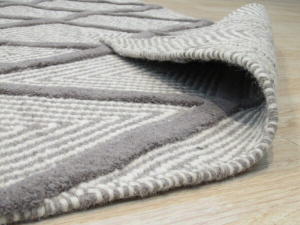 Close-up of a rolled gray rug featuring raised geometric lines on a textured striped weave on light wood.