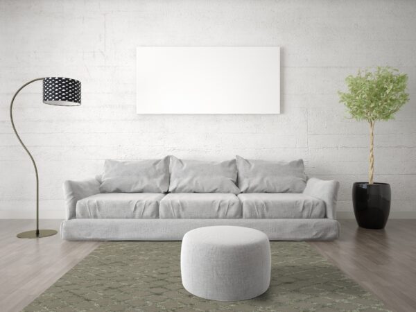 A muted green lattice rug anchors a grey sofa and ottoman against a white textured wall and wood floor.