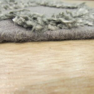Low-angle view of a gray rug showing contrasting short and shaggy textures on wood.
